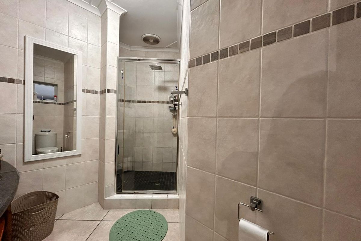 A functional bathroom featuring a glass-enclosed shower, tiled walls with decorative border, and a wall-mounted mirror.