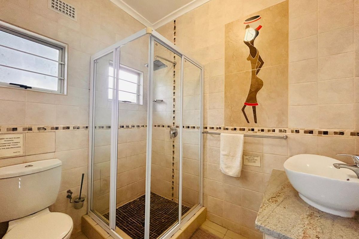 A functional bathroom featuring a glass-enclosed shower, a vessel sink on a stone vanity, and a toilet, finished with neutral wall tiles and decorative accents.