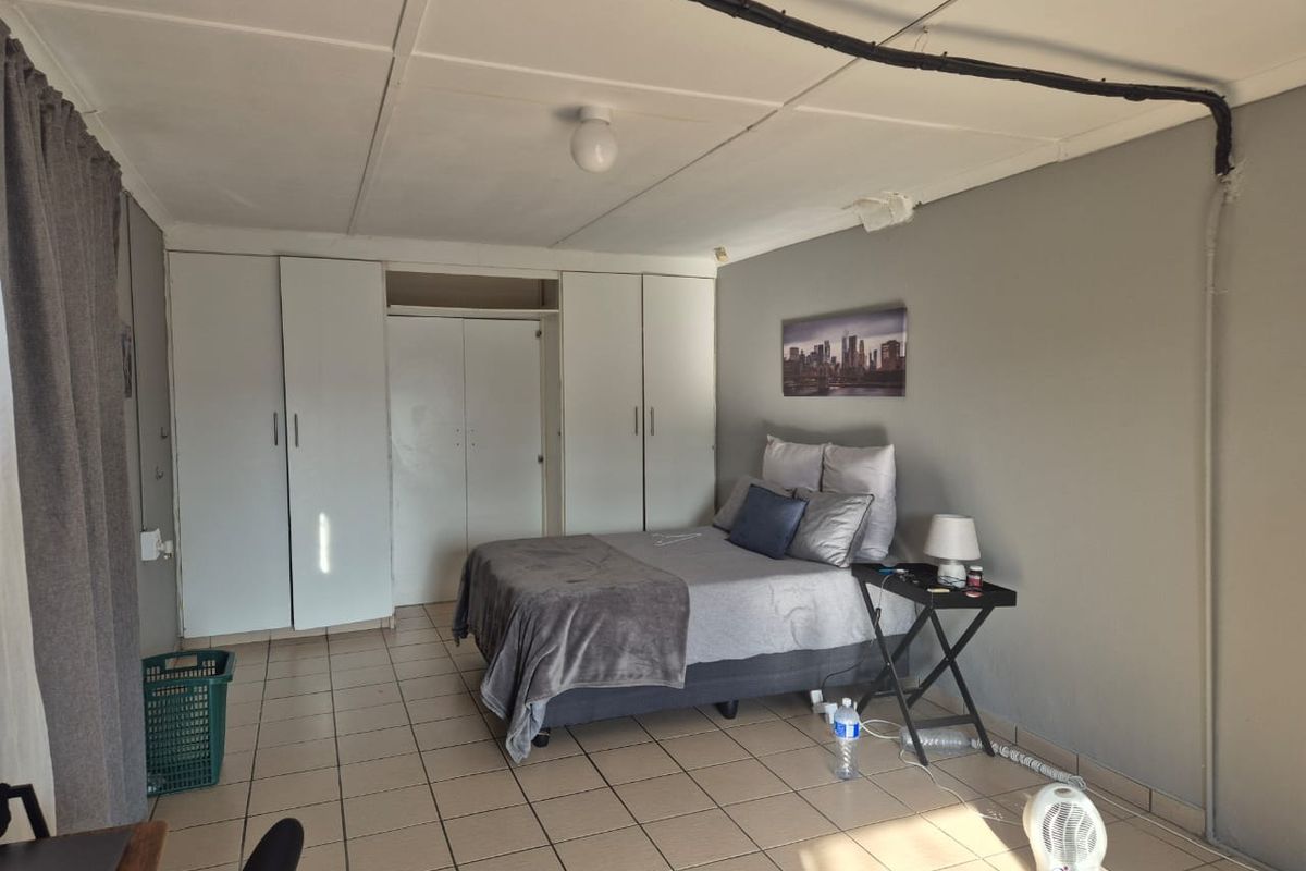 A bedroom featuring built-in wardrobes, tiled flooring, and exposed electrical conduit along the ceiling.
