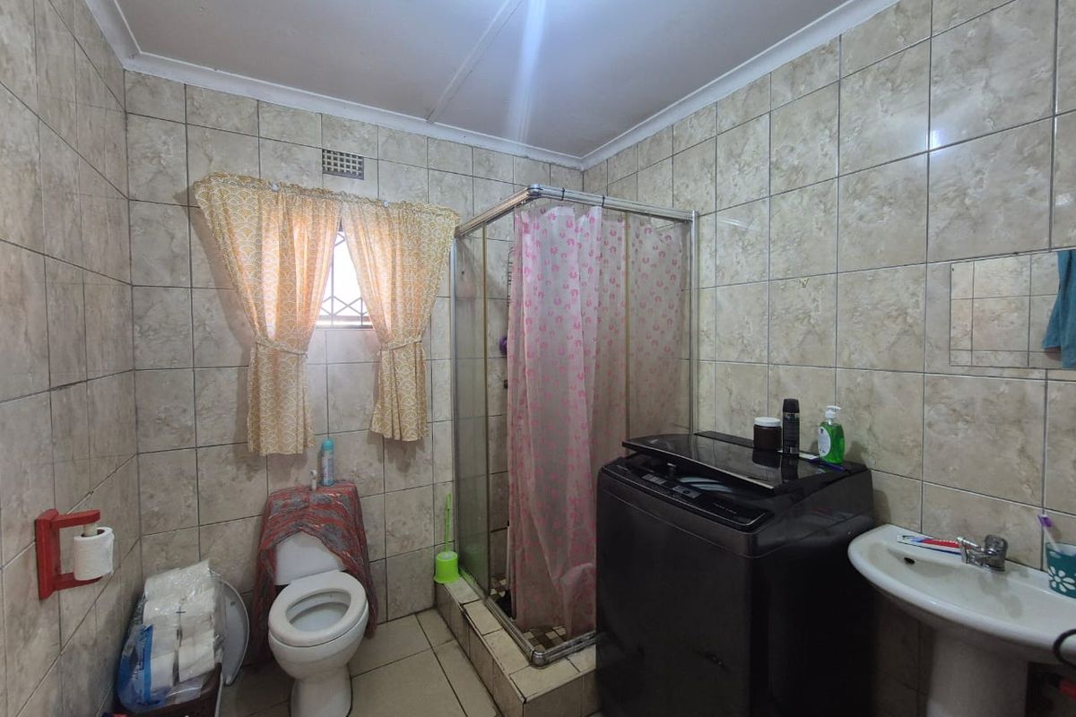 A functional bathroom featuring a corner shower enclosure, pedestal basin, and toilet, finished with full-height wall tiling.