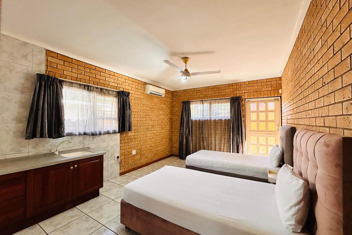 Spacious bedroom featuring exposed brick walls, tiled flooring, a built-in vanity with sink, air conditioning unit, and direct access to the exterior.