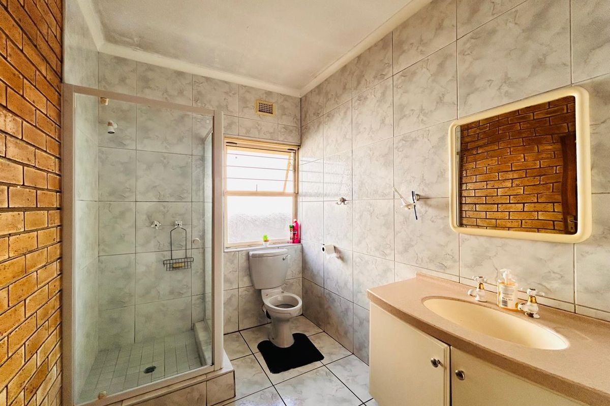 A functional bathroom featuring a glass-enclosed shower, a built-in vanity with basin, and a toilet, finished with neutral wall and floor tiling.