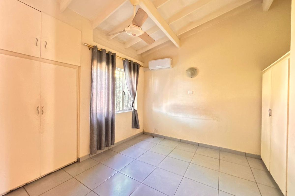 A bedroom featuring tiled flooring, built-in cabinetry, a ceiling fan, and a wall-mounted air conditioning unit under a vaulted ceiling.