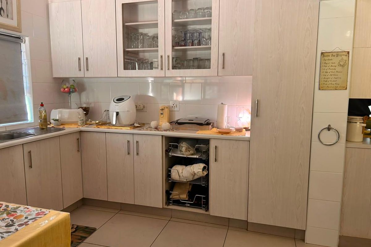A functional kitchen featuring light wood-grain laminate cabinetry, glass-fronted display units, tiled backsplash, and practical pull-out storage solutions.