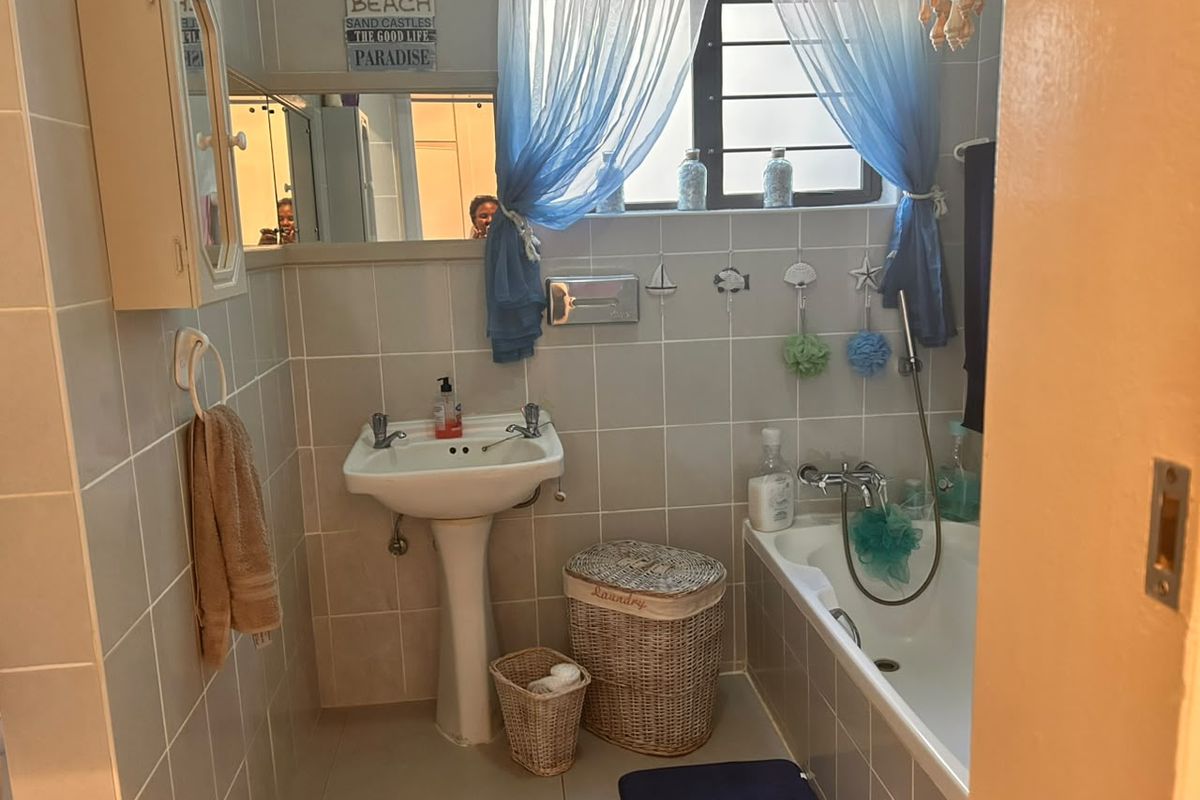 A functional bathroom featuring a pedestal basin, built-in bathtub with handheld shower, and neutral wall tiling throughout.