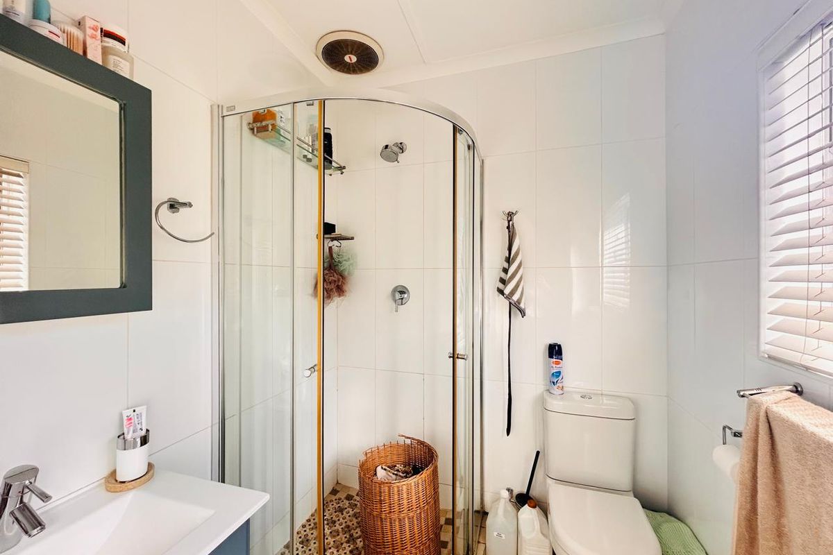 A functional bathroom featuring a corner shower enclosure, a modern vanity basin, and a standard toilet with white wall tiling.