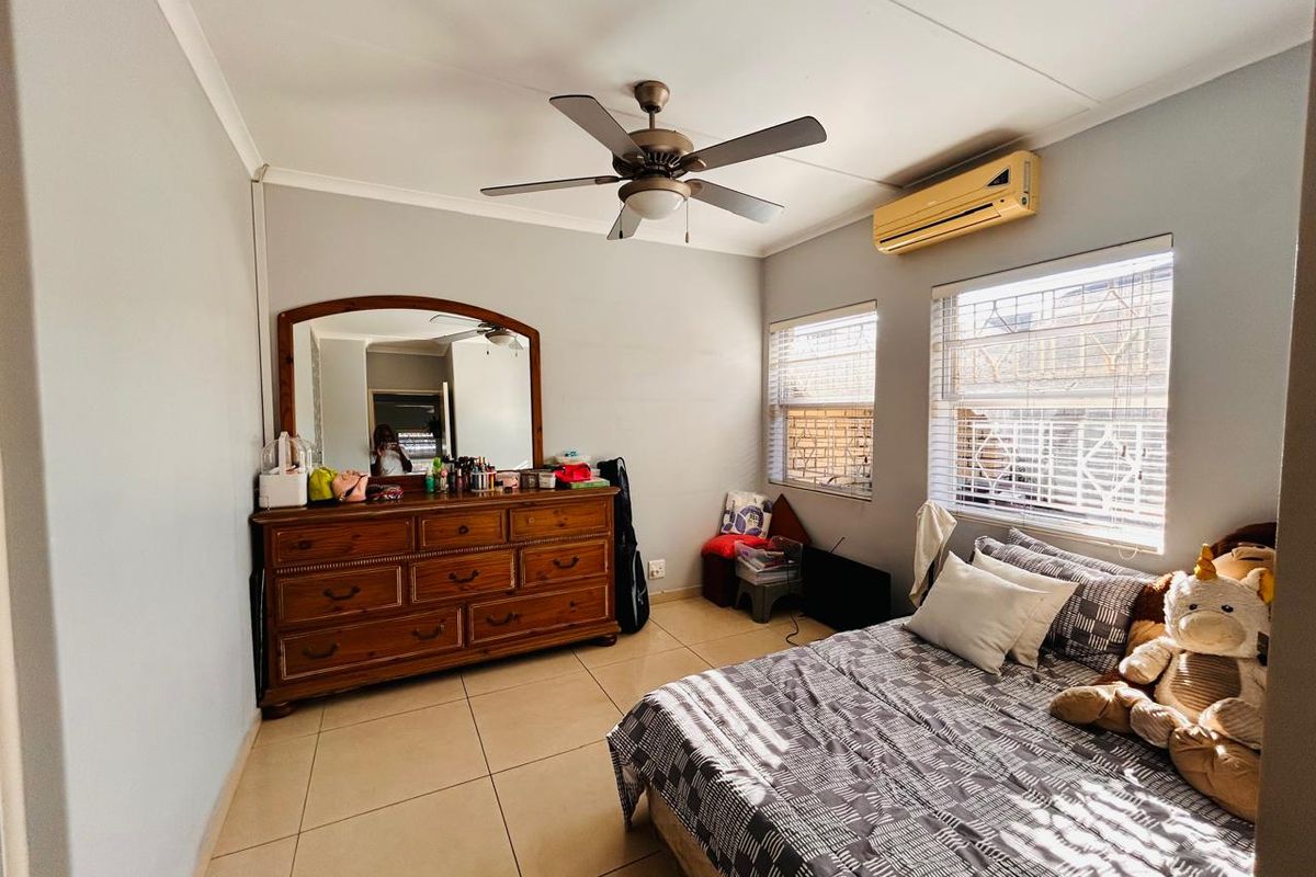 A bedroom featuring tiled flooring, a ceiling fan, and a wall-mounted air conditioning unit with security bars on the windows.