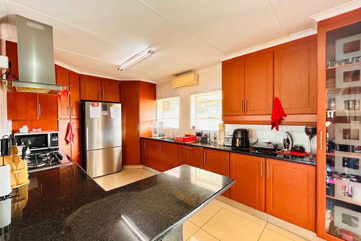 A functional kitchen featuring warm wooden cabinetry, granite countertops, a gas hob, and a stainless steel extractor fan, offering ample storage and workspace.