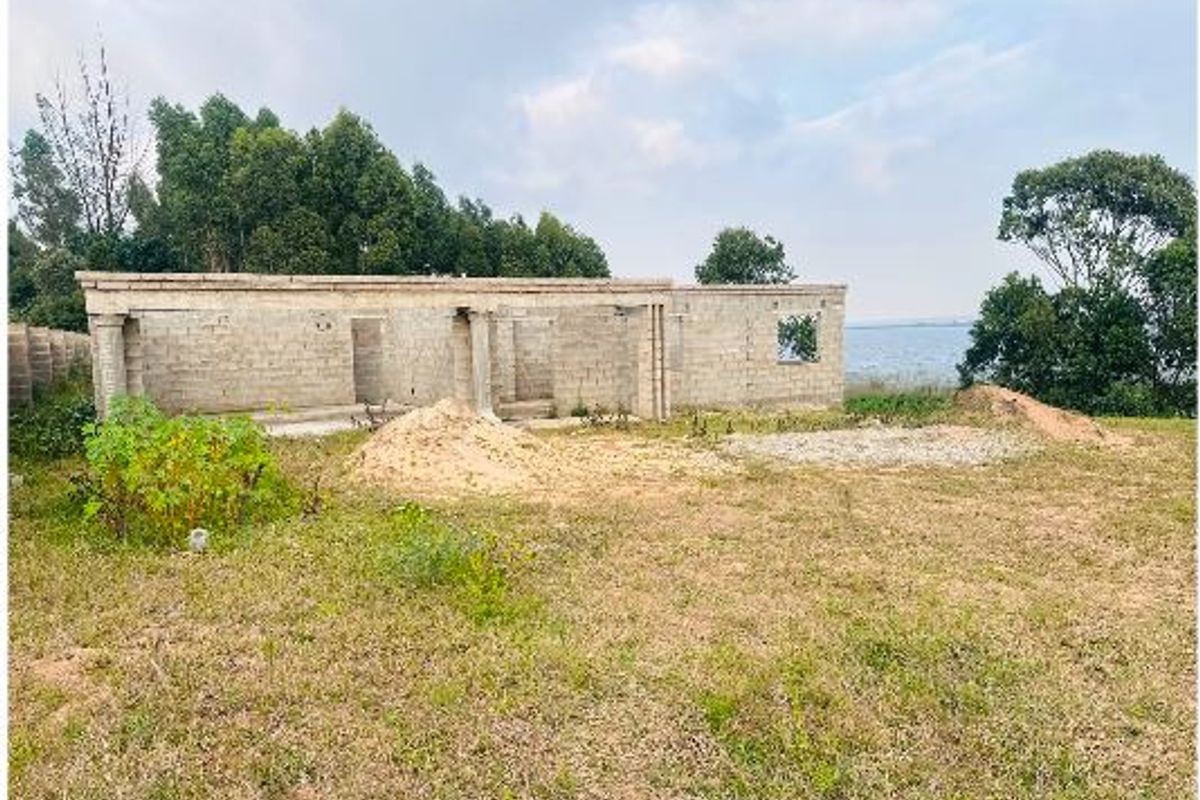 An unfinished residential structure in shell condition, featuring concrete block walls and columns, situated on a large plot of land with water views.
