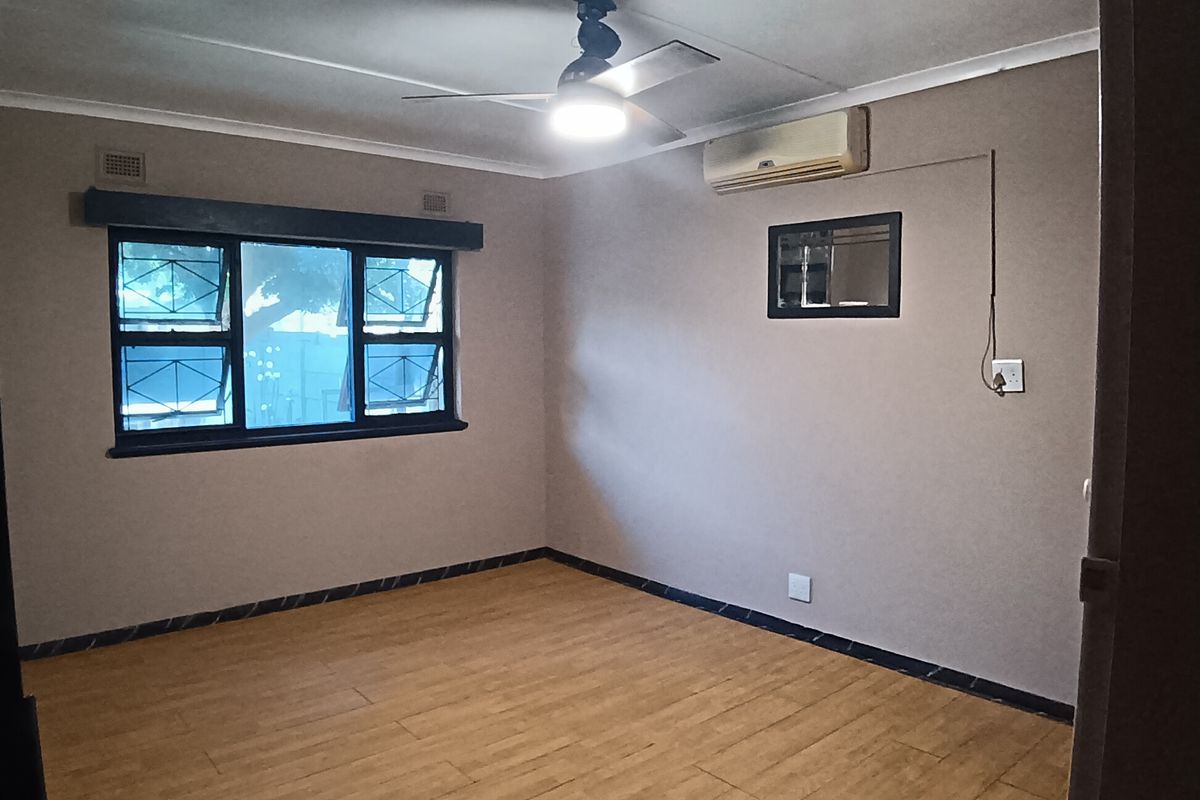 An empty bedroom featuring laminate flooring, a ceiling fan, and a wall-mounted air conditioning unit.