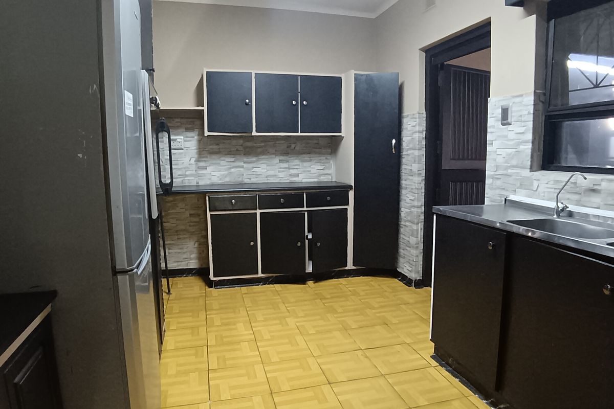 A functional kitchen featuring dark built-in cabinetry, tiled backsplash, and a stainless steel sink, offering a practical layout with potential for modern updates.