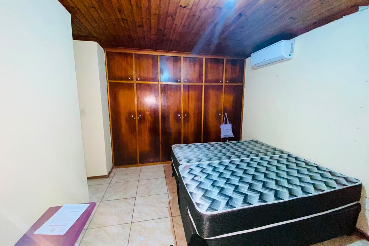 A bedroom featuring built-in wooden cupboards, a timber ceiling, and a split-system air conditioner with tiled flooring.