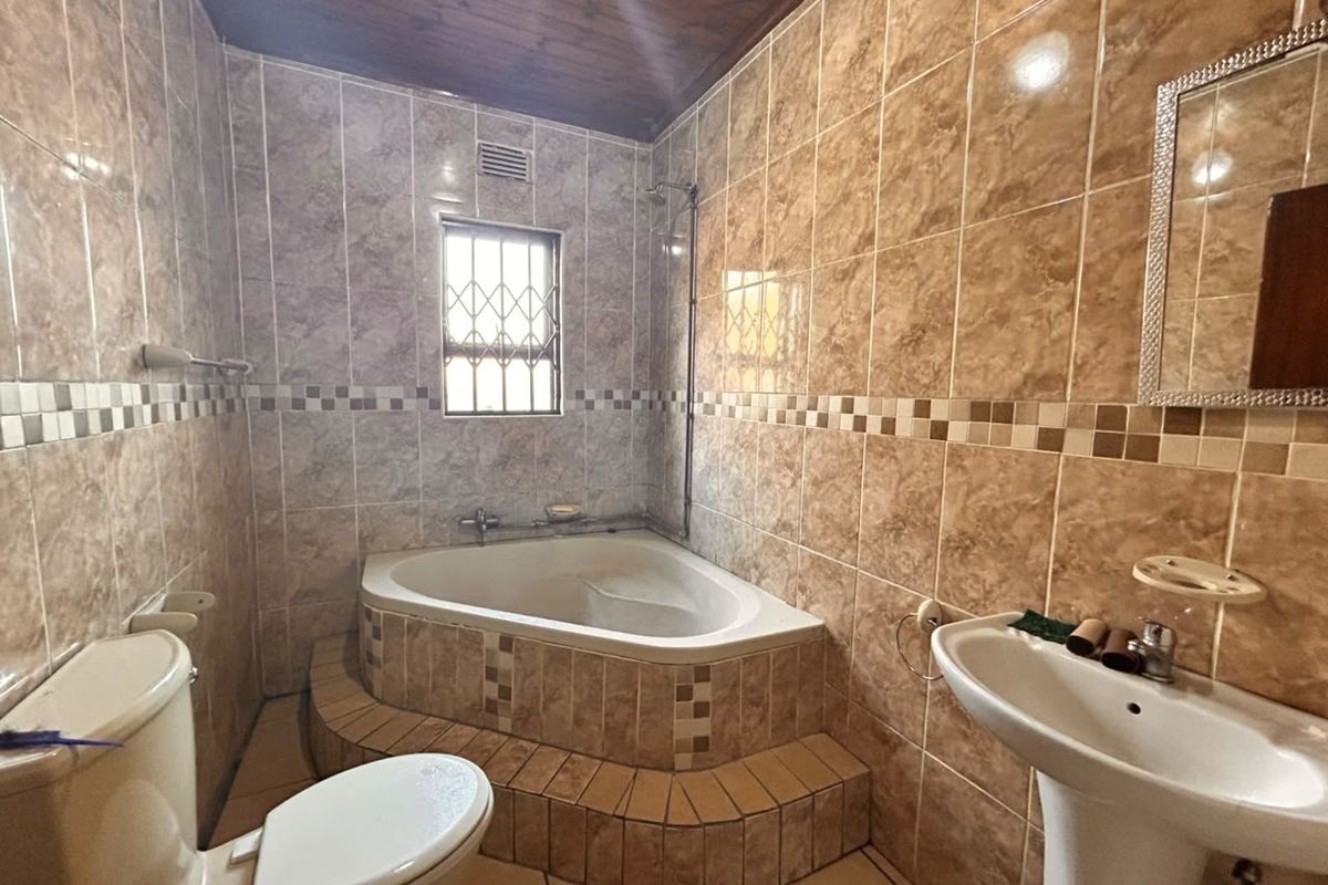 A functional bathroom featuring a corner bathtub, pedestal sink, toilet, and full-height wall tiling with a timber ceiling finish.