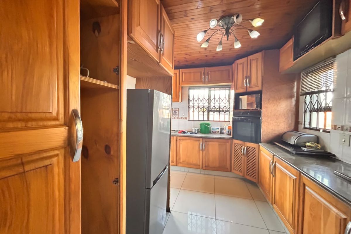 A functional kitchen featuring extensive wooden cabinetry, built-in oven and microwave, tiled flooring, and a timber-paneled ceiling with security bars on the windows.