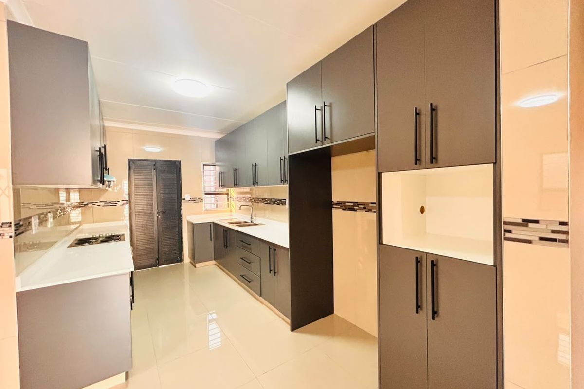 Modern kitchen featuring sleek dark grey cabinetry, white stone countertops, integrated hob, and neutral tiled finishes throughout.