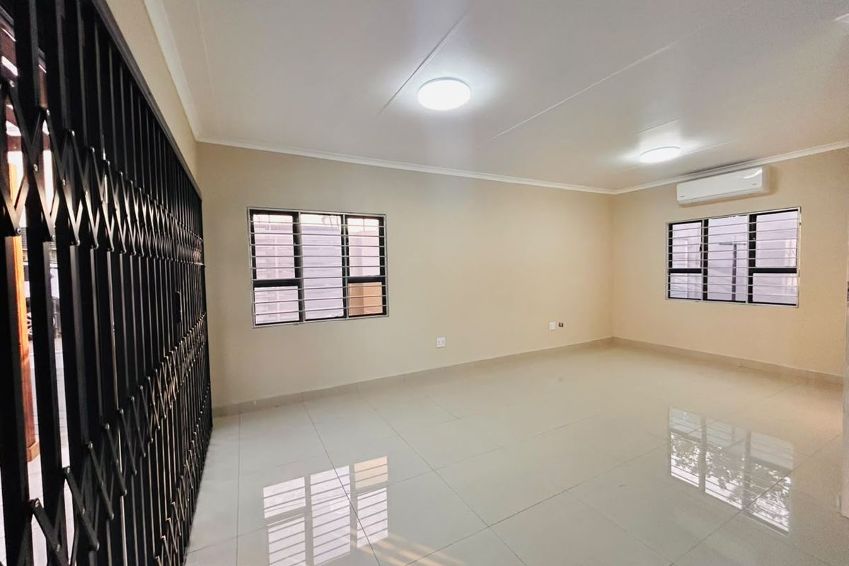 A spacious, empty living area featuring tiled floors, air conditioning, and secure aluminium windows with security bars.