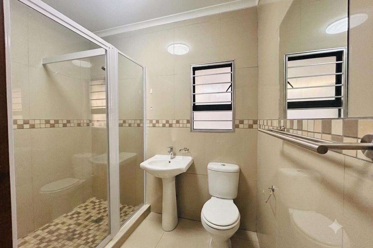 A clean, functional bathroom featuring a pedestal basin, a separate shower enclosure with glass doors, and neutral wall tiling.
