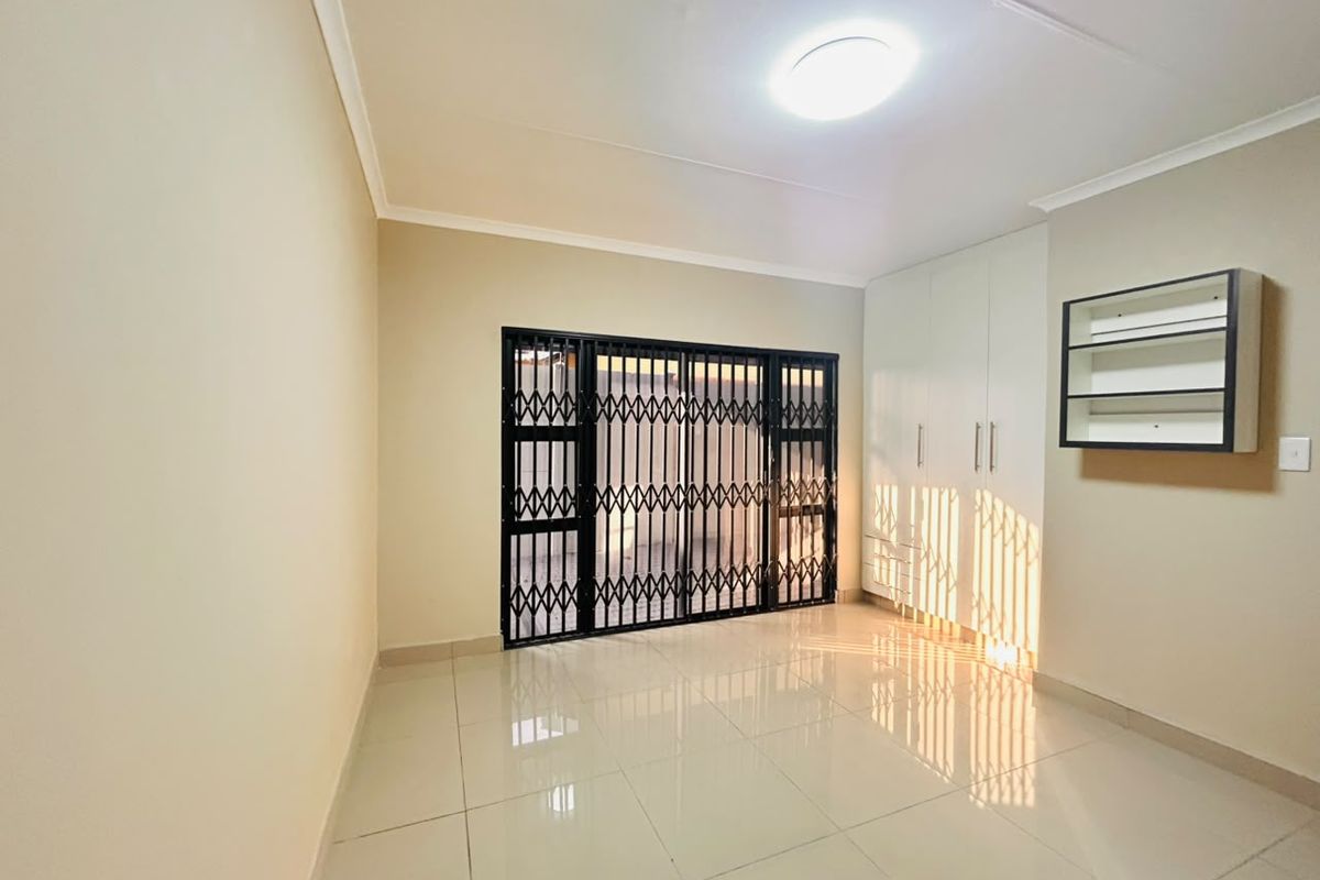 A bright, empty bedroom featuring tiled flooring, built-in cupboards, and a secure metal gate leading to the exterior.