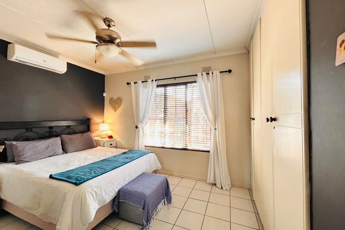 A bedroom featuring tiled flooring, built-in cupboards, a ceiling fan, and a wall-mounted air conditioning unit.