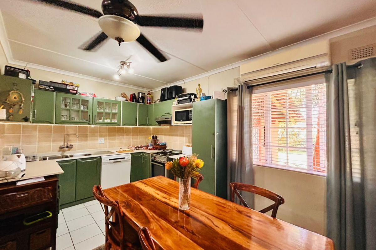A functional kitchen featuring green cabinetry, tiled backsplash, built-in appliances, and a ceiling fan, with an adjacent dining area and window security bars.