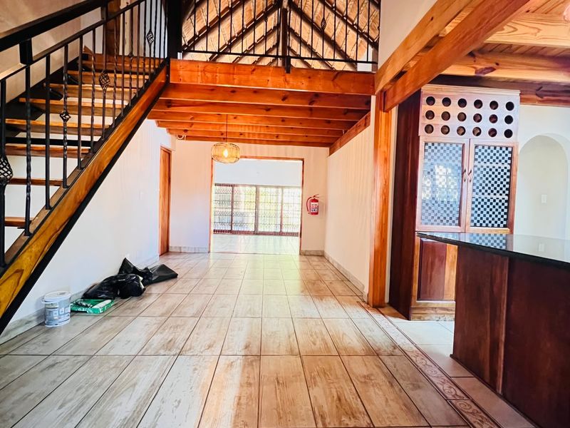 Spacious open-plan living area featuring high vaulted thatched ceilings, exposed timber beams, a wrought iron staircase, and built-in cabinetry with granite surfaces.