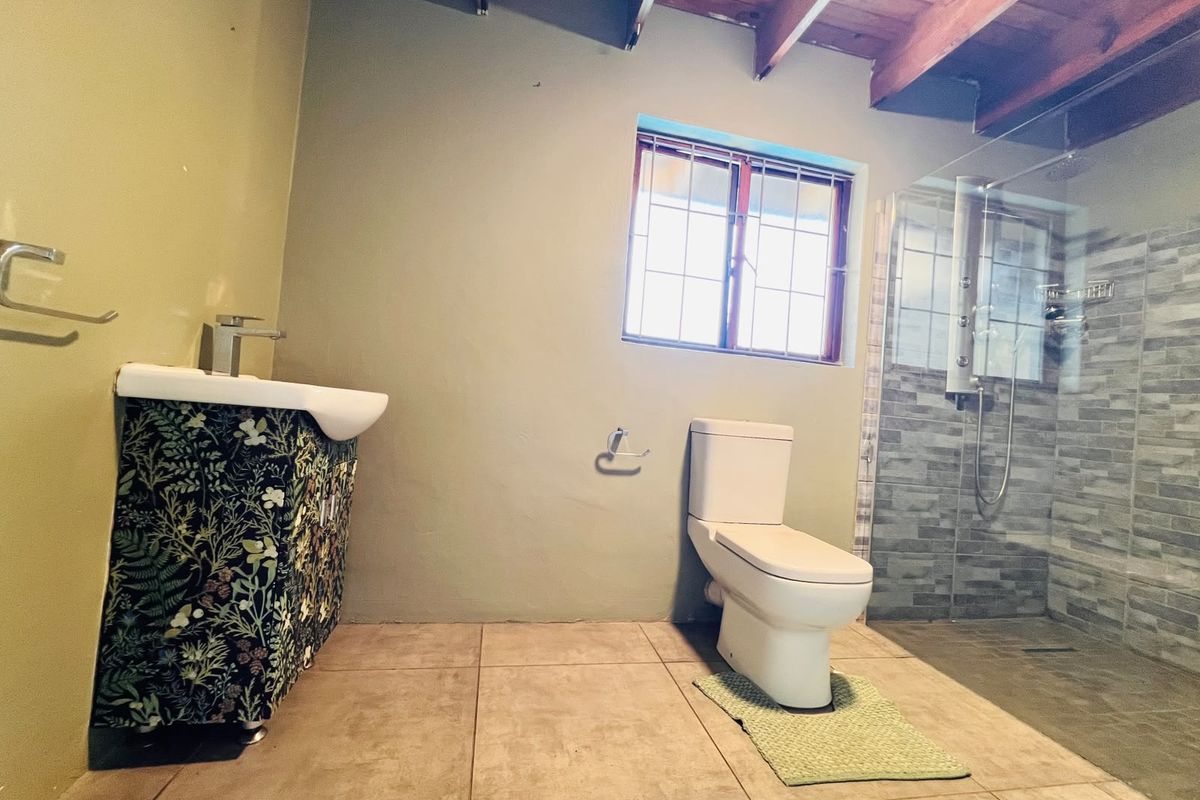 A modern bathroom featuring a glass-enclosed shower, tiled flooring, a vanity basin, and exposed timber ceiling beams.