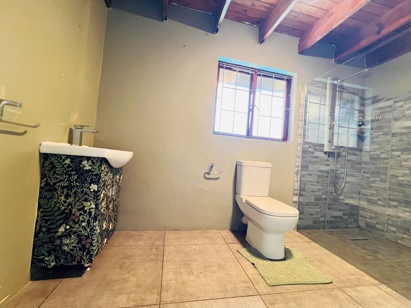 A modern bathroom featuring a glass-enclosed shower, tiled flooring, a vanity basin, and exposed timber ceiling beams.