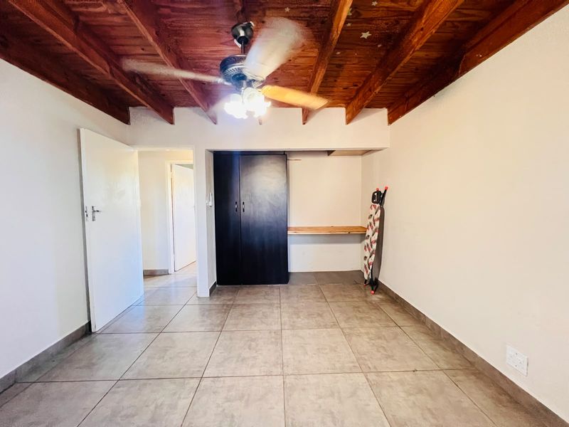 A bedroom featuring tiled flooring, an exposed timber beam ceiling with a ceiling fan, and a built-in wardrobe with an integrated desk area.
