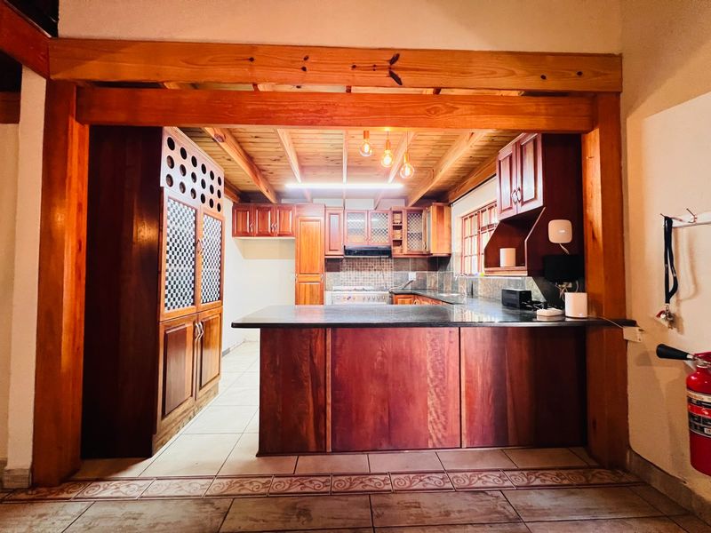 A rustic kitchen featuring extensive timber cabinetry, granite countertops, a central island, and exposed wooden ceiling beams with warm lighting.