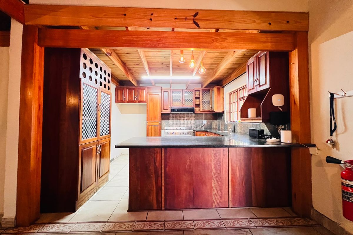 A rustic kitchen featuring extensive timber cabinetry, granite countertops, a central island, and exposed wooden ceiling beams with warm lighting.