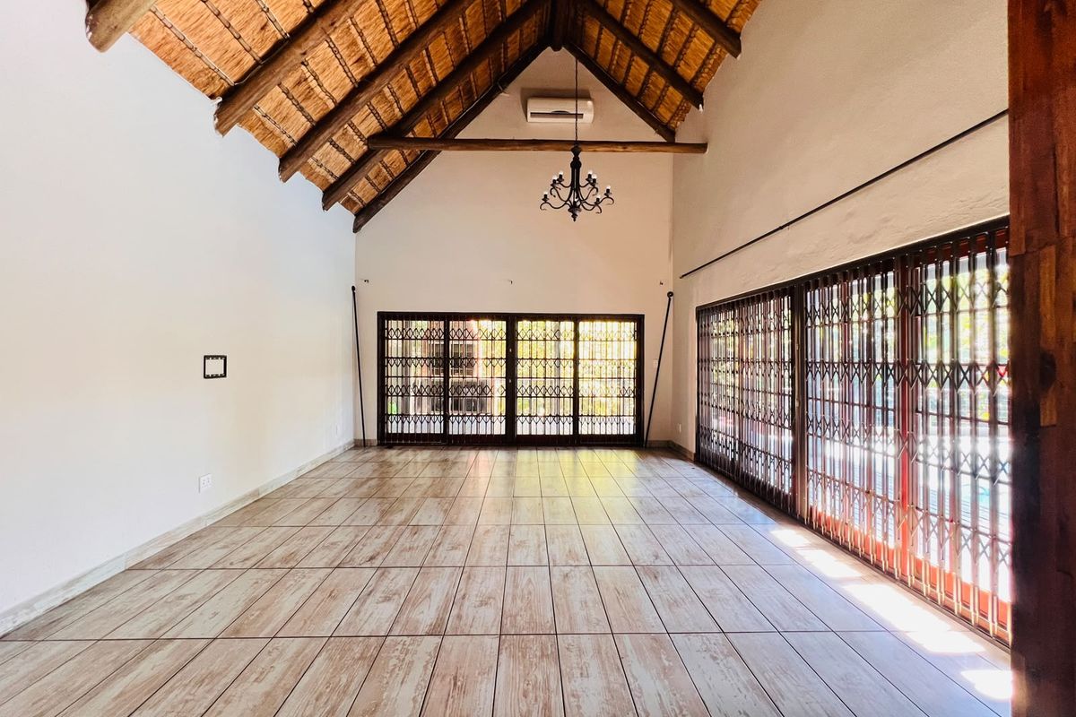 Spacious living area featuring a high vaulted thatched ceiling with exposed timber trusses, ceramic tile flooring, and large sliding doors with security gates.