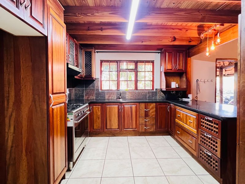 Spacious kitchen featuring warm timber cabinetry, exposed ceiling beams, granite countertops, and a gas stove, offering a classic and functional cooking space.