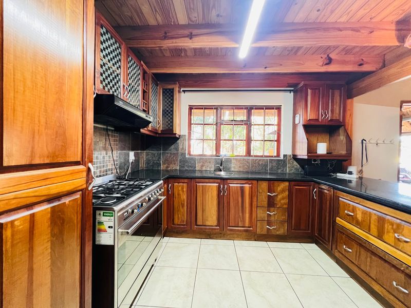 A rustic kitchen featuring warm wooden cabinetry, granite countertops, a gas stove with extractor, and exposed timber ceiling beams.