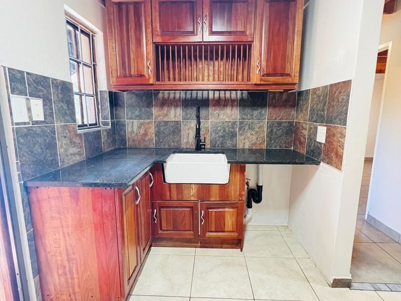 A functional scullery area featuring wooden cabinetry, granite countertops, a farmhouse sink, and exposed timber ceiling beams.