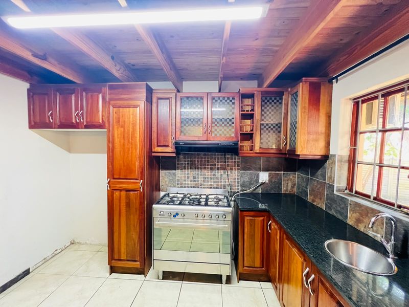 A functional kitchen featuring warm wooden cabinetry, granite countertops, a gas stove with extractor, and a distinctive exposed wooden beam ceiling.