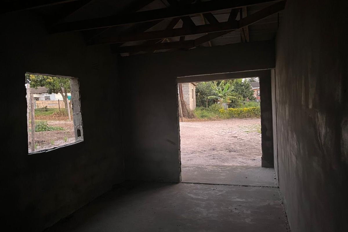 An unfinished interior space featuring exposed timber roof trusses, plastered masonry walls, and a cement screed floor, awaiting final finishes and fixtures.