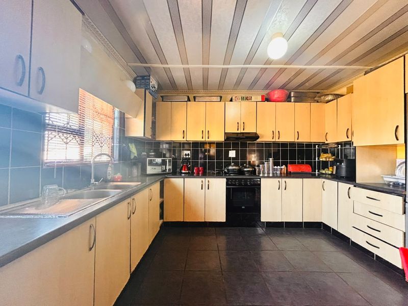 A functional kitchen featuring light wood-look cabinetry, black tiled backsplash, double sink, and built-in oven with extractor fan.