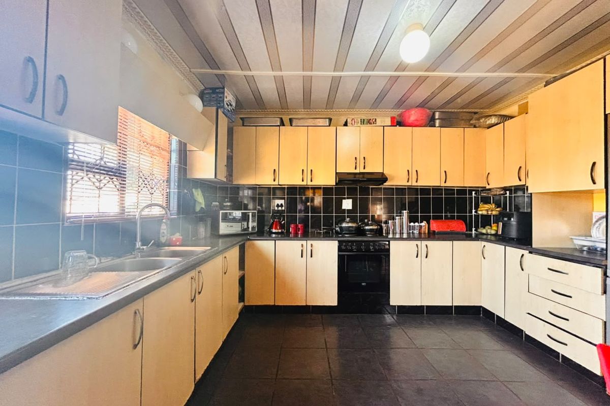 A functional kitchen featuring light wood-look cabinetry, black tiled backsplash, double sink, and built-in oven with extractor fan.