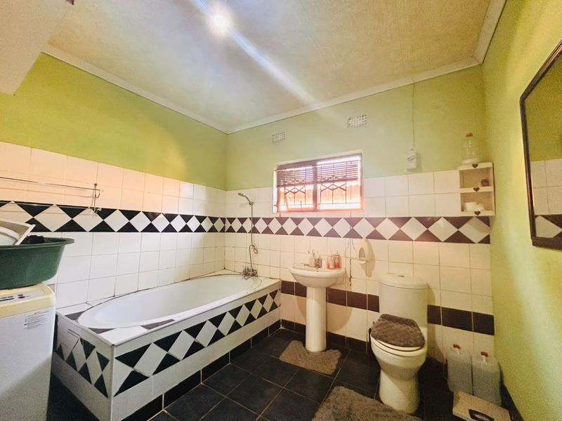 A functional bathroom featuring a bathtub, pedestal sink, and toilet, finished with dated black and white patterned wall tiles.