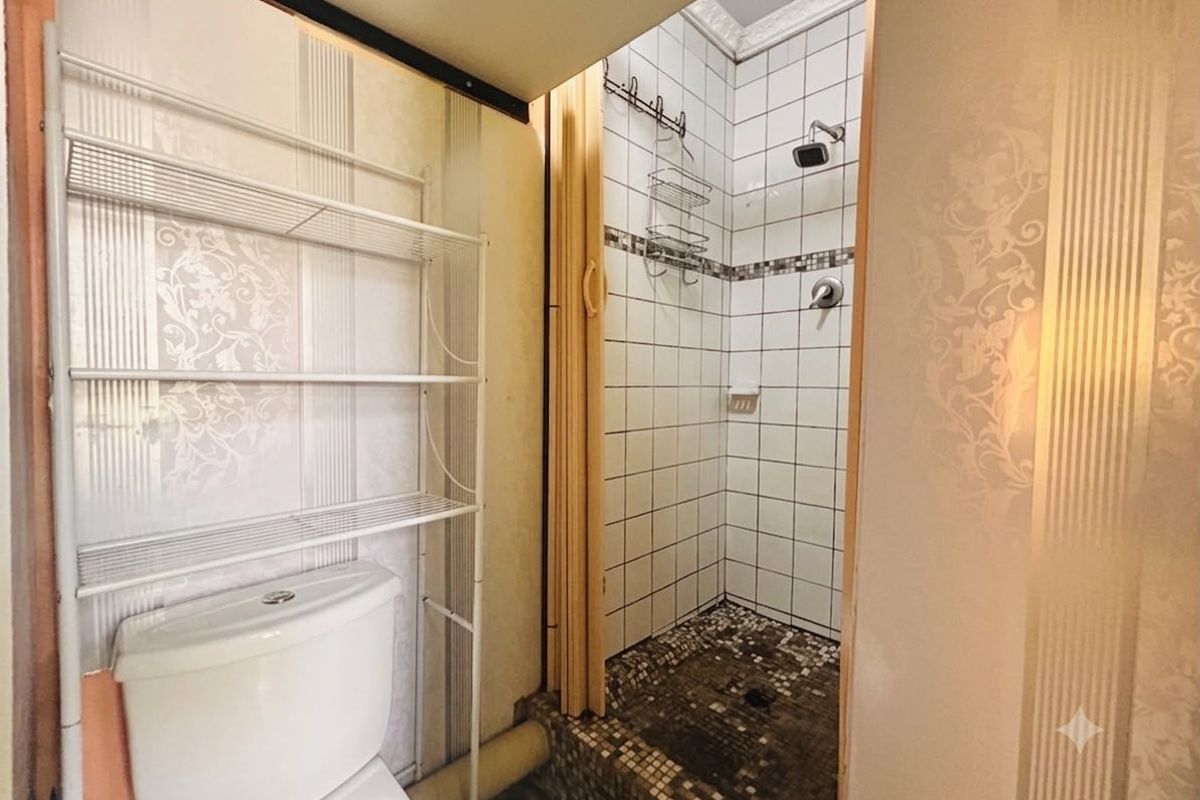 A compact bathroom featuring a tiled shower enclosure with mosaic flooring and a standard toilet, requiring cosmetic updates to modernize the space.