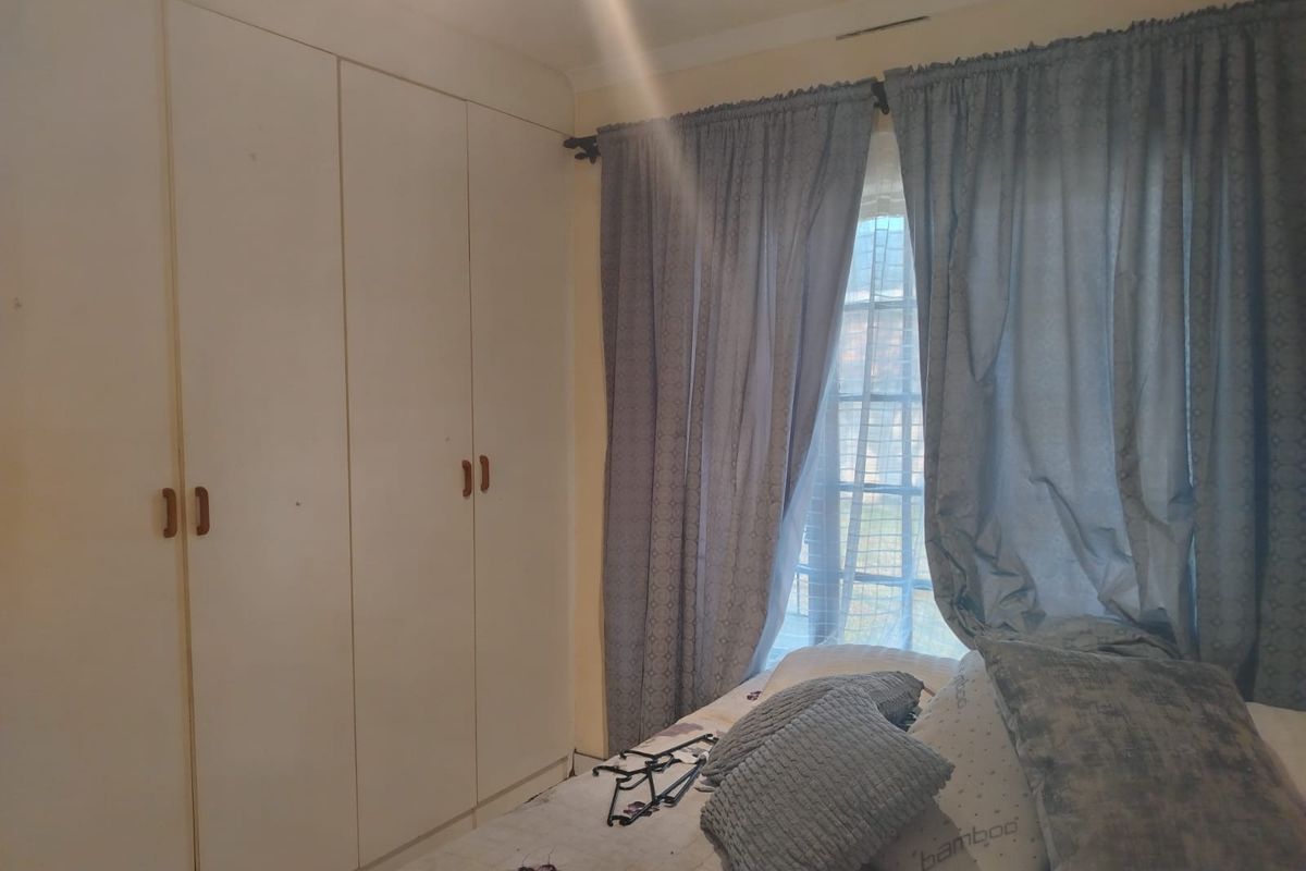 A bedroom featuring built-in cupboards and a window with curtaining.