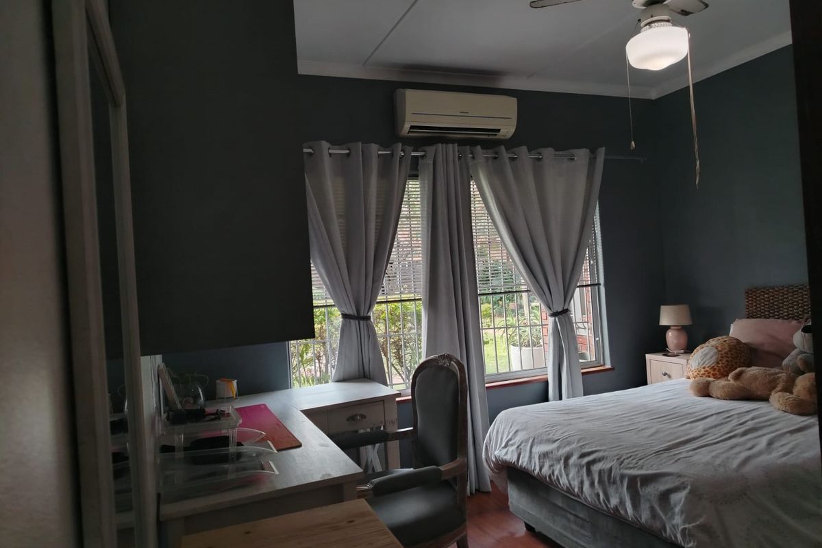 A bedroom featuring dark painted walls, wood-look flooring, a ceiling fan, and a wall-mounted air conditioning unit.