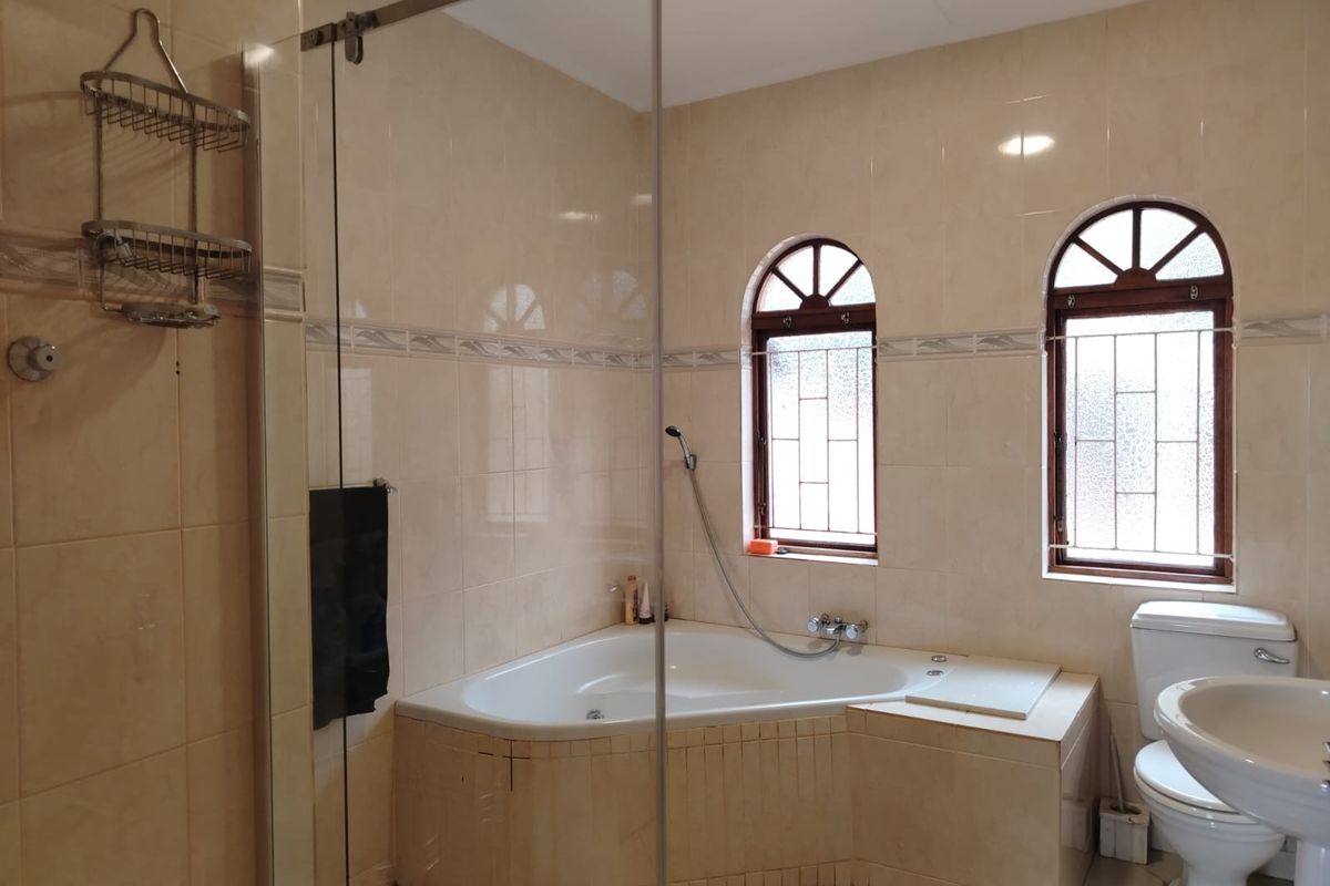 A bathroom featuring a corner bathtub, a glass-enclosed shower, and arched windows with security bars.
