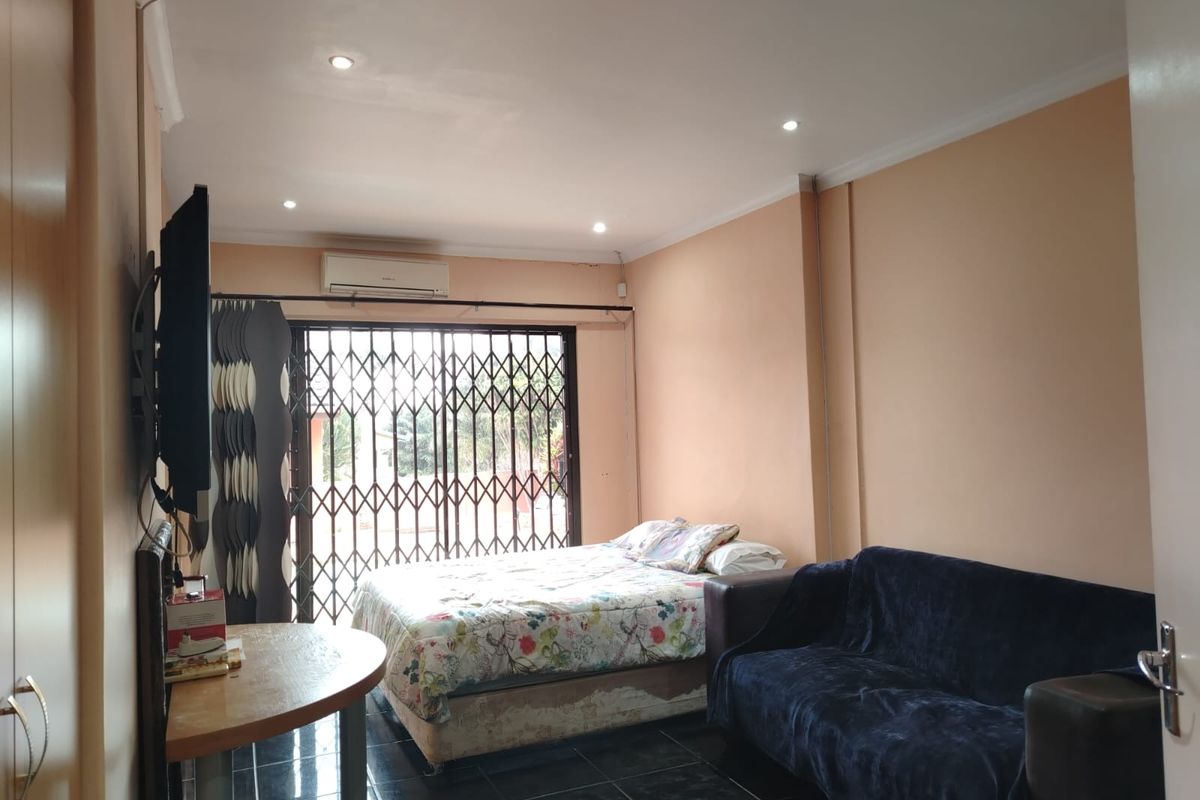 A functional bedroom featuring tiled flooring, recessed ceiling lighting, a wall-mounted air conditioning unit, and a security gate leading to the exterior.