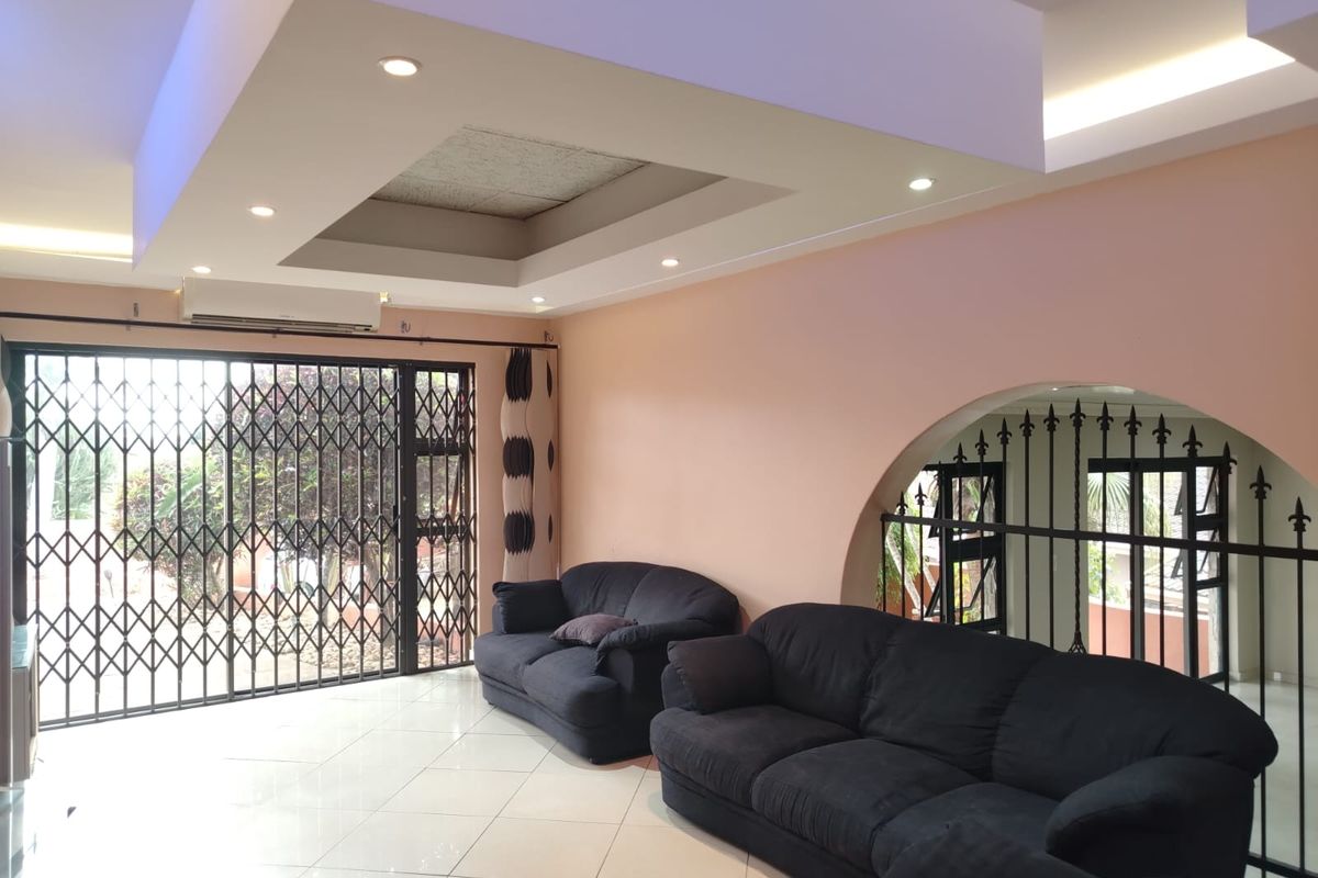 Spacious living room featuring a recessed tray ceiling with integrated downlighting, tiled flooring, and secure metal security gates leading to the exterior.