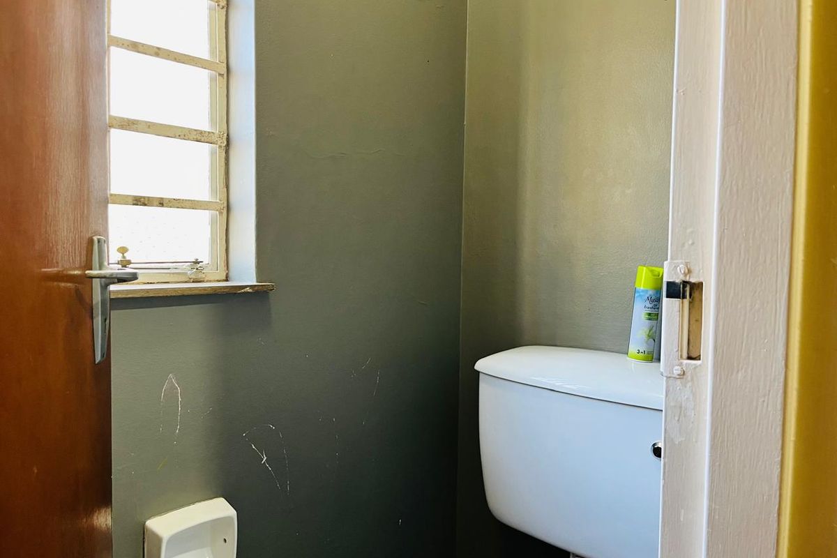 A compact guest toilet featuring a standard white toilet suite and a window with security bars.