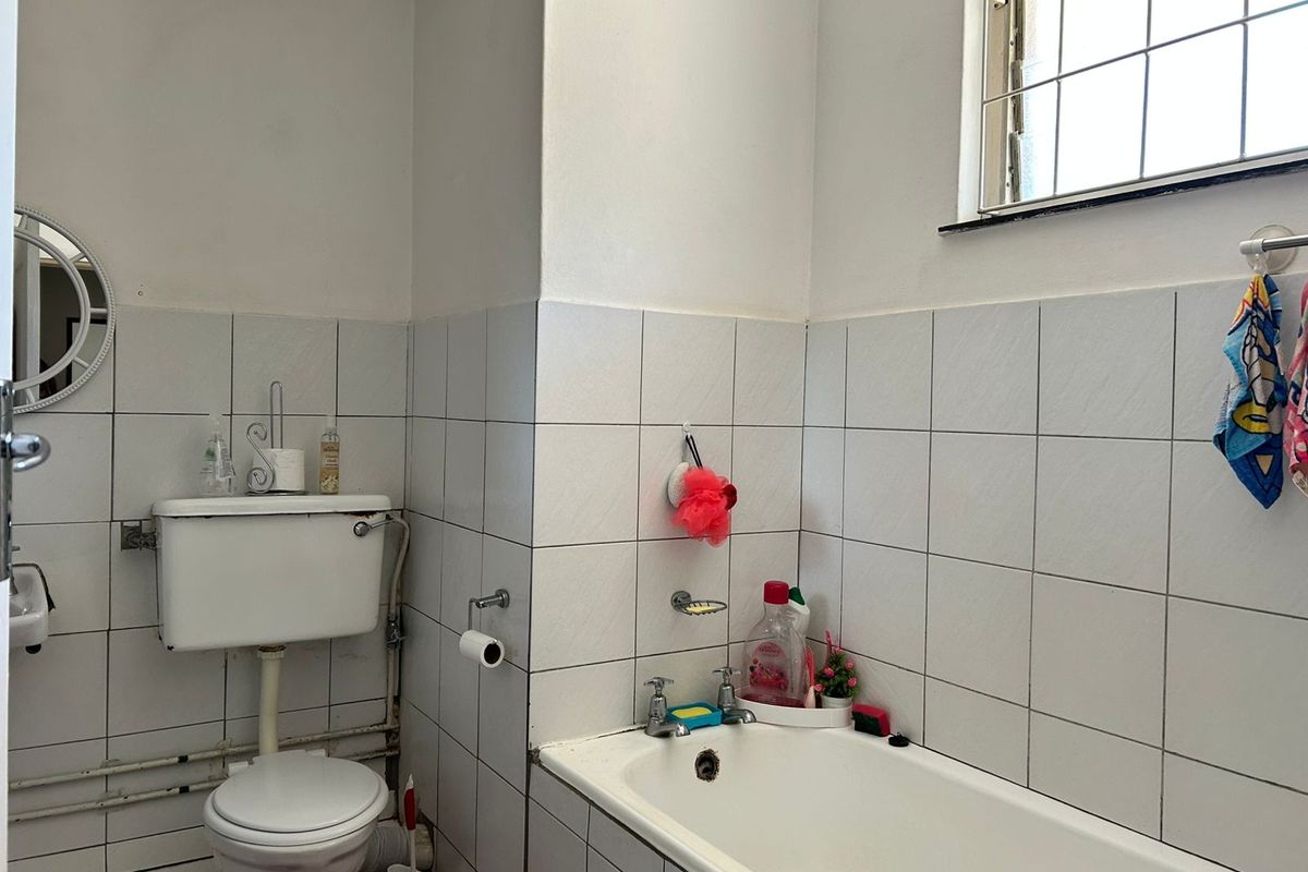 A functional bathroom featuring a standard bathtub, toilet, and tiled walls with a security-barred window.