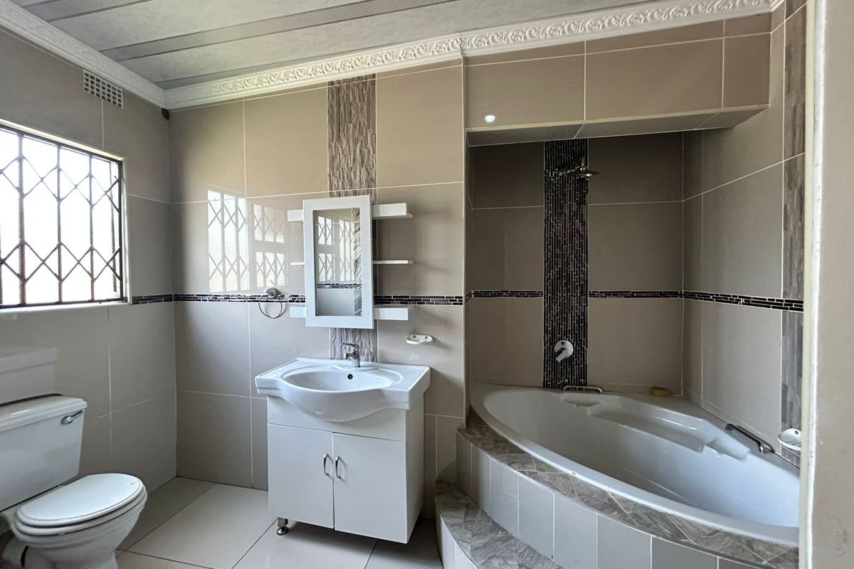A well-maintained bathroom featuring a built-in corner bathtub, a modern vanity with integrated sink, and floor-to-ceiling wall tiling.