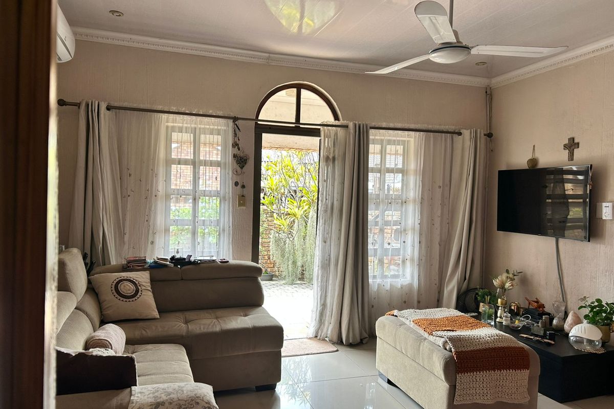 A comfortable living room featuring tiled flooring, a ceiling fan, and an arched glass door providing direct access to the outdoor patio area.