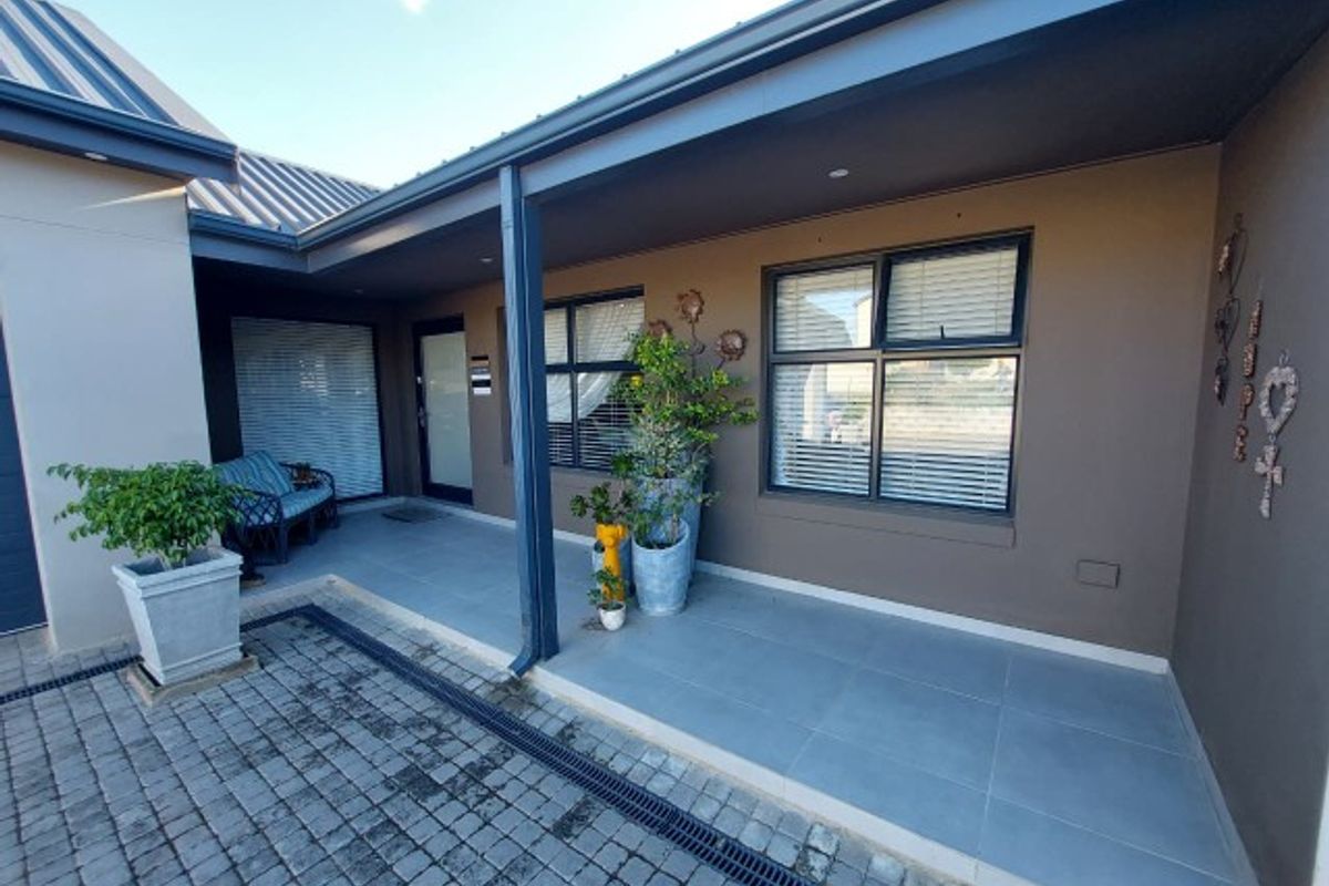 A covered patio area featuring tiled flooring, aluminium window frames, and a paved driveway with an integrated drainage channel.